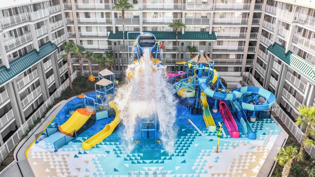 A water park with multiple slides and water features, surrounded by a multi-story building with balconies. - Holiday Inn Resort Orlando Suites - Waterpark by IHG (Orlando)