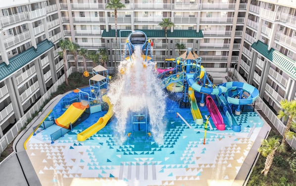 Un parc aquatique doté de nombreux toboggans et d’attractions aquatiques, entouré d’un immeuble à plusieurs étages avec des balcons.
