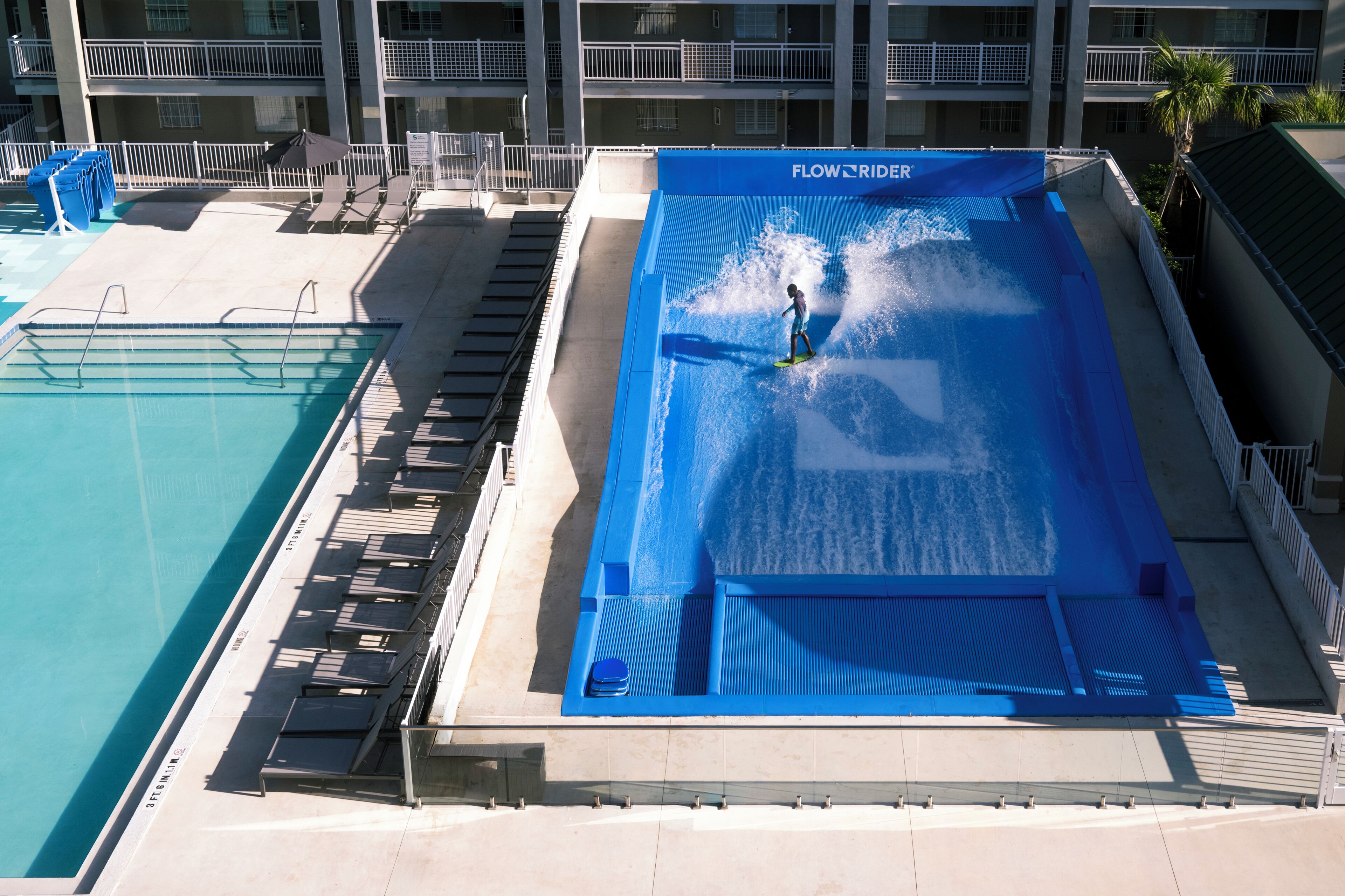 Un tobogán acuático con una persona en la parte superior, una piscina y un edificio con balcones.