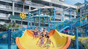 A water park with a yellow slide, blue and yellow water features, and a multi-level building with balconies in the background. - Holiday Inn Resort Orlando Suites - Waterpark by IHG (Orlando)
