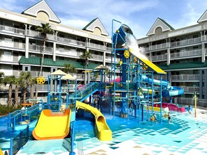 Ein Wasserpark mit Rutschen und Wasserspielen, umgeben von einem mehrstöckigen Hotel mit Balkonen.