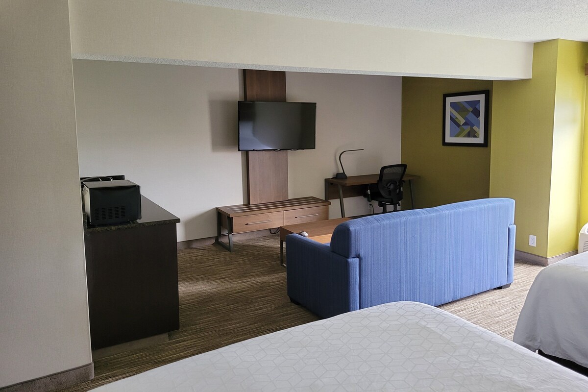 A hotel room with a bed, a desk with a chair, a television, and a small cabinet.