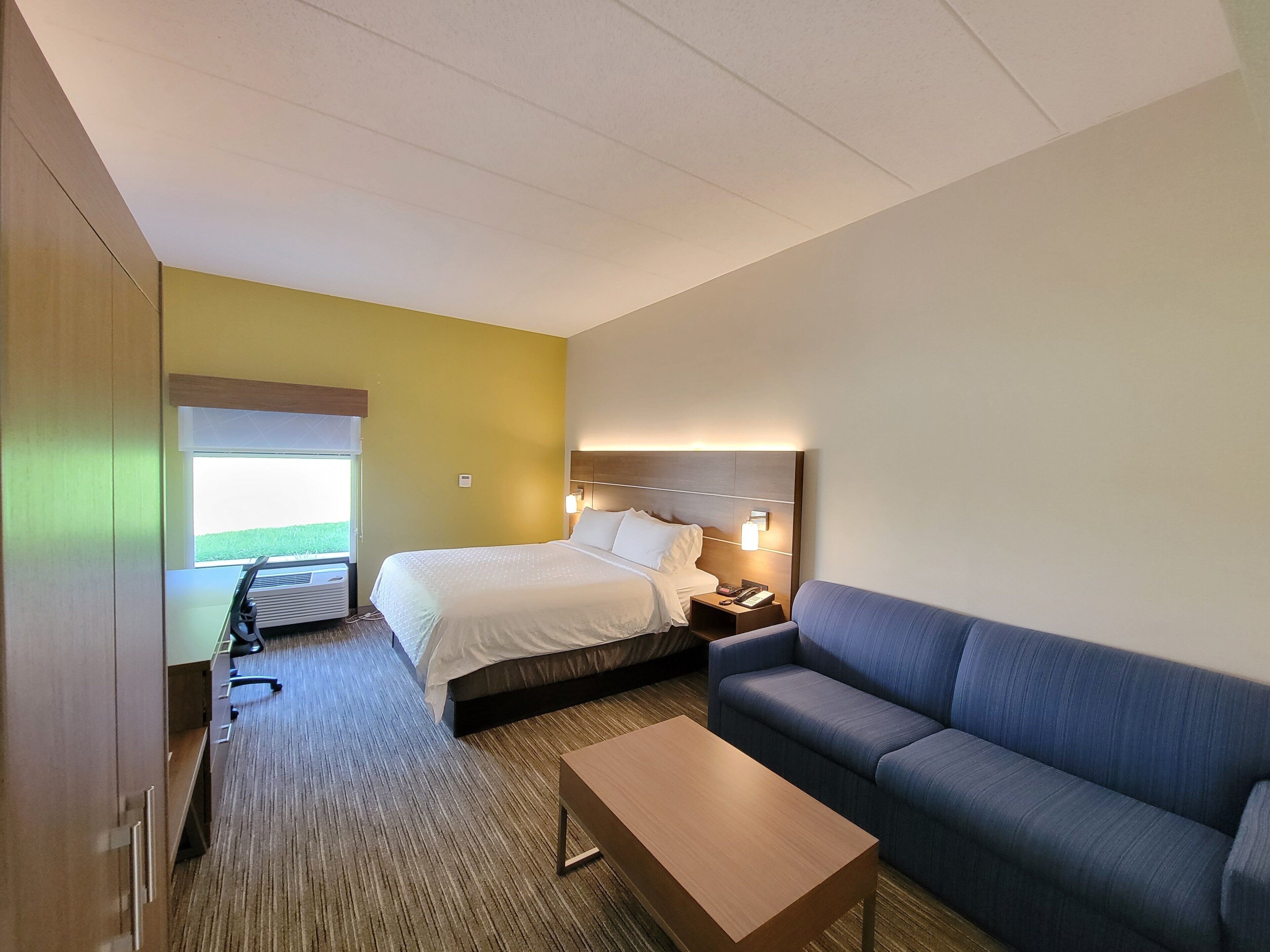 Habitación de hotel con cama, sofá, una mesita y ventana con vistas a un campo verde.