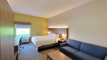 Habitación de hotel con cama, sofá, una mesita y ventana con vistas a un campo verde.