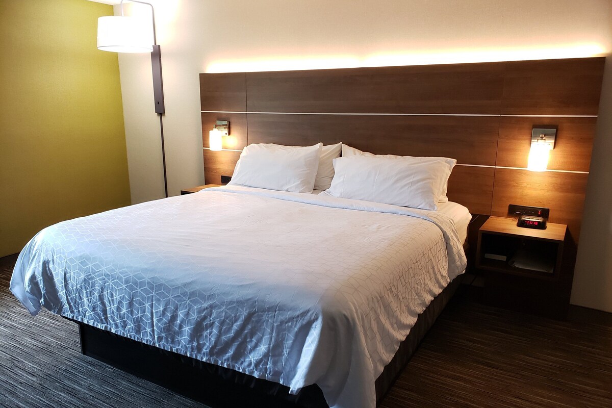 A hotel room with a large bed, two bedside tables, a nightstand, and a wall-mounted light fixture.