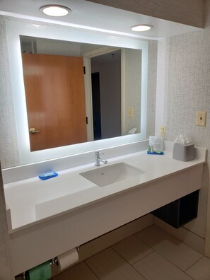 A bathroom with a white sink, a mirror, and a towel dispenser. - Holiday Inn Express Edgewood-Aberdeen-Bel Air by IHG (Edgewood)