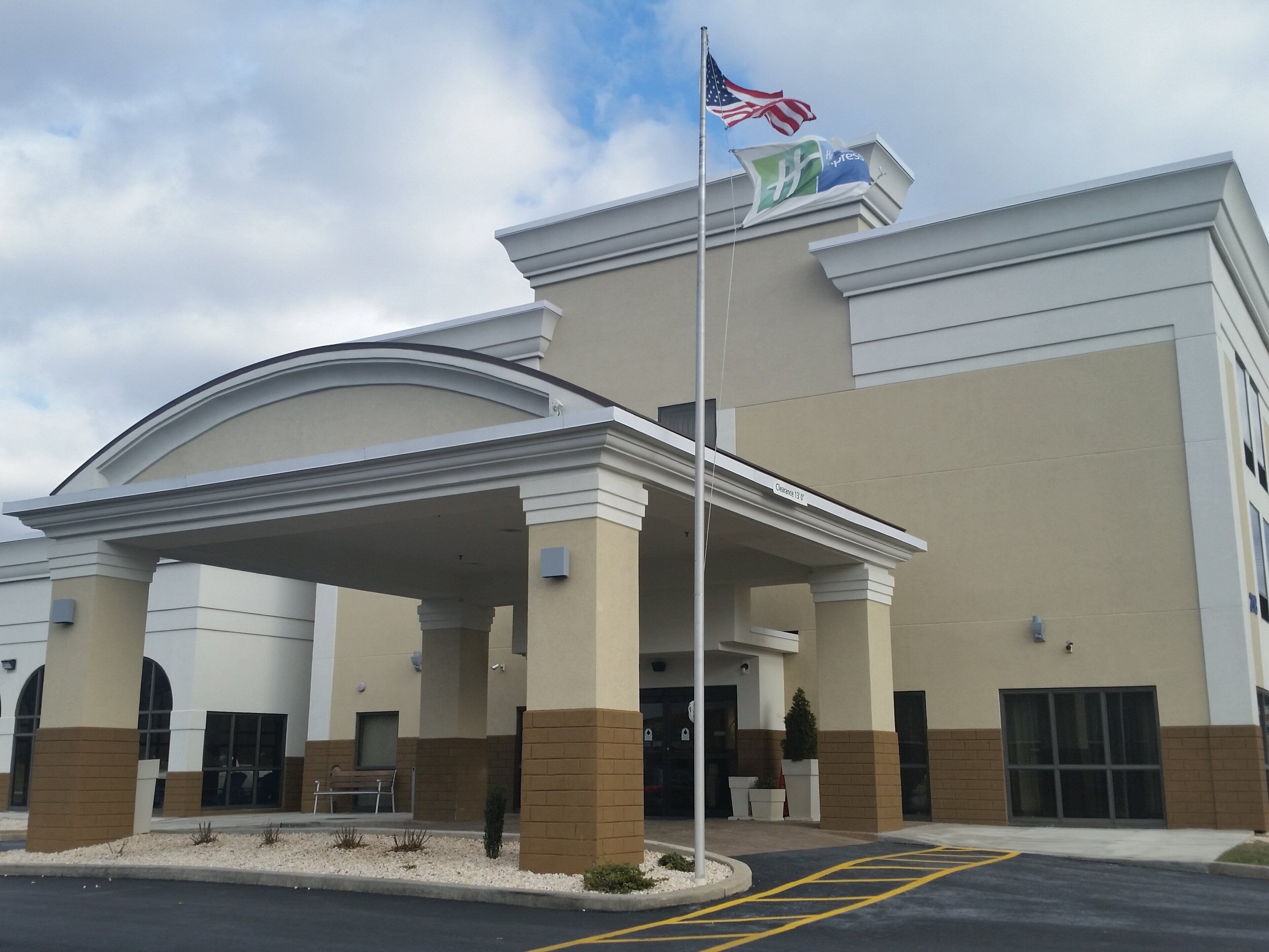 A hotel entrance with a covered area, a flagpole with flags, and a parking lot.