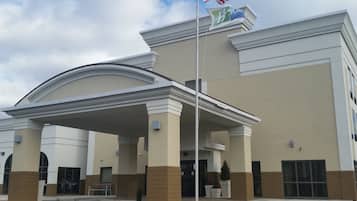 A hotel entrance with a covered area, a flagpole with flags, and a parking lot.