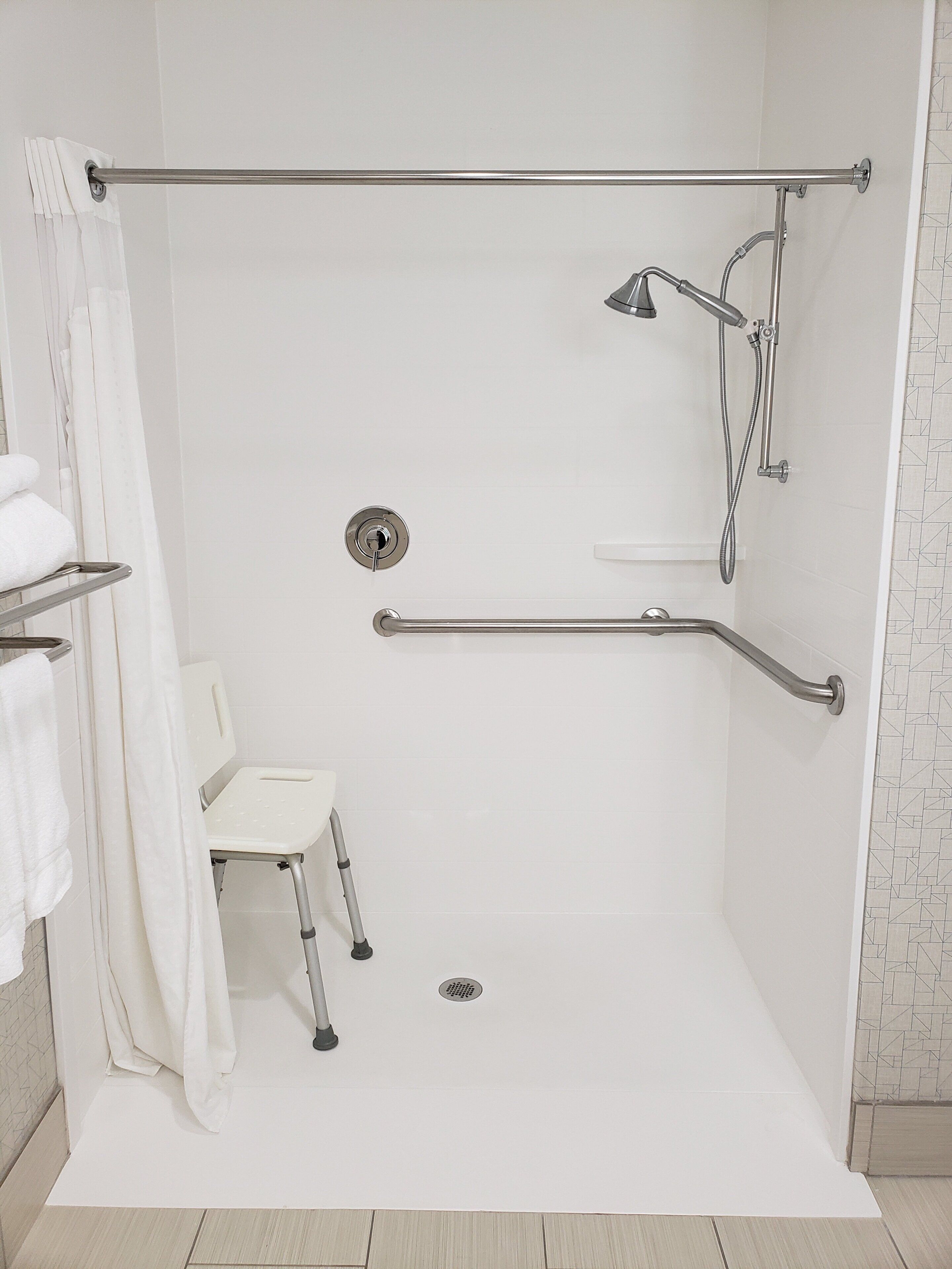 A white shower with a grab bar, a white chair, and a towel rack.
