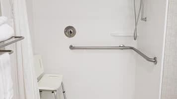 Baño blanco con barra de apoyo, asiento de ducha y toallero.