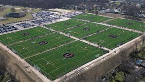 Luchtbeeld van een sportcomplex met verschillende voetbalvelden, parkeerplaatsen en gebouwen.