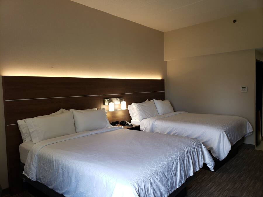 Habitació d'hotel amb dos llits, un panell de fusta al capçal, làmpades laterals i un termòstat a la paret.