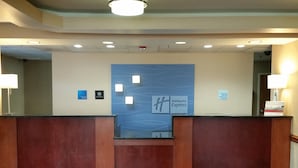 Un comptoir d’accueil d’hôtel avec un mur bleu orné du logo de Holiday Inn Express, un panneau indiquant les heures d’arrivée et de départ, et un panneau indiquant qu’il est interdit d’amener des animaux.