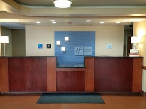 A hotel reception desk with a blue wall featuring the Holiday Inn Express logo, a check-in/out sign, and a 'No Pets' sign. - Holiday Inn Express Edgewood-Aberdeen-Bel Air by IHG (Edgewood)