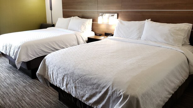 Een hotelkamer met twee bedden, een nachtkastje met een lamp en een houten hoofdeinde.
