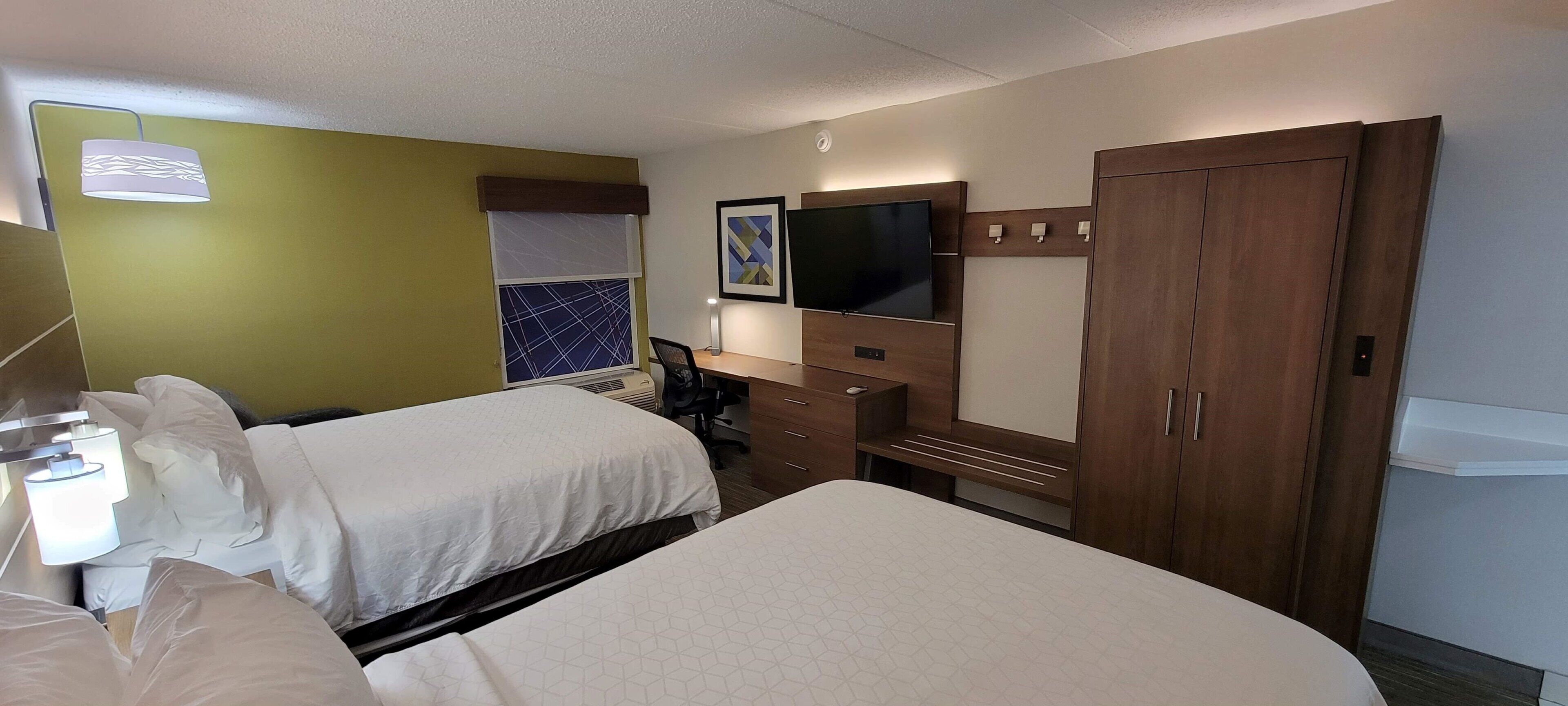 A hotel room with two beds, a desk, a chair, a television, and a wardrobe.