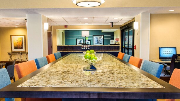 A conference room with a long table, blue and orange chairs, and a reception desk in the background.