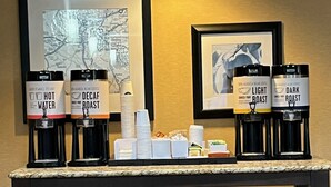 A coffee station with labeled dispensers for hot water, decaf roast, light roast, and dark roast coffee.