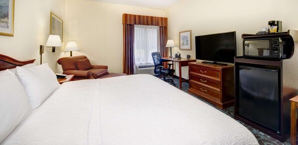 Habitación de hotel con una cama grande, un escritorio con televisor, microondas y una silla.