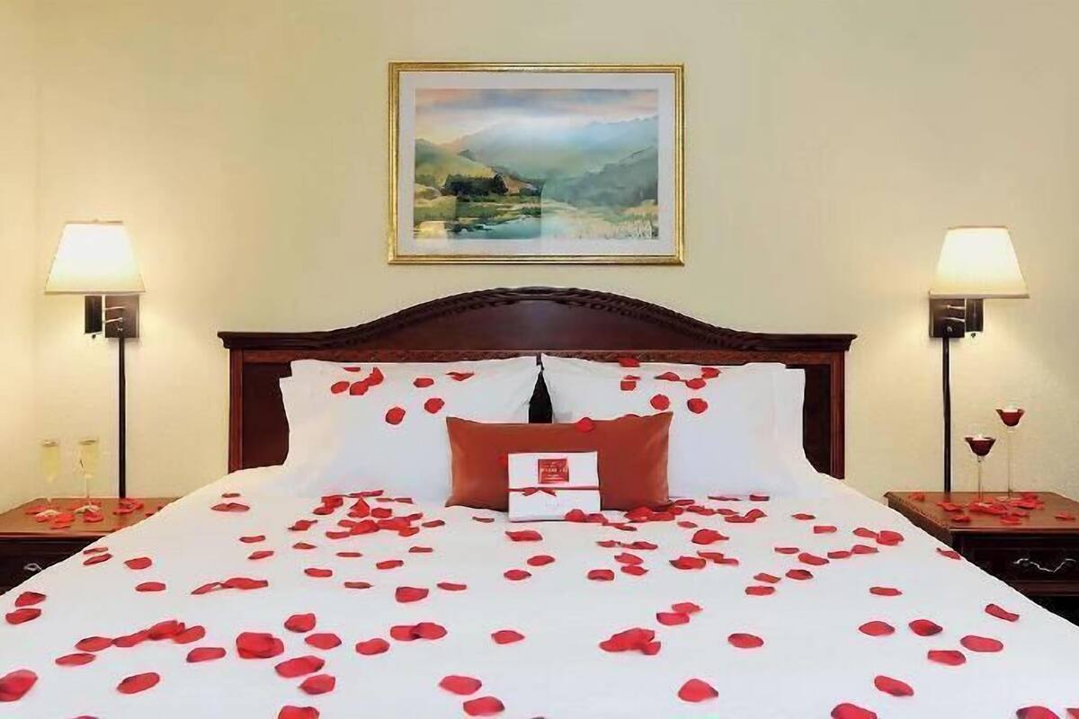A hotel room with a large bed, two bedside tables, a nightstand, a painting on the wall, and two lamps.