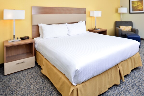 Una habitación de hotel con una cama grande, dos mesitas de noche, una silla y una lámpara.