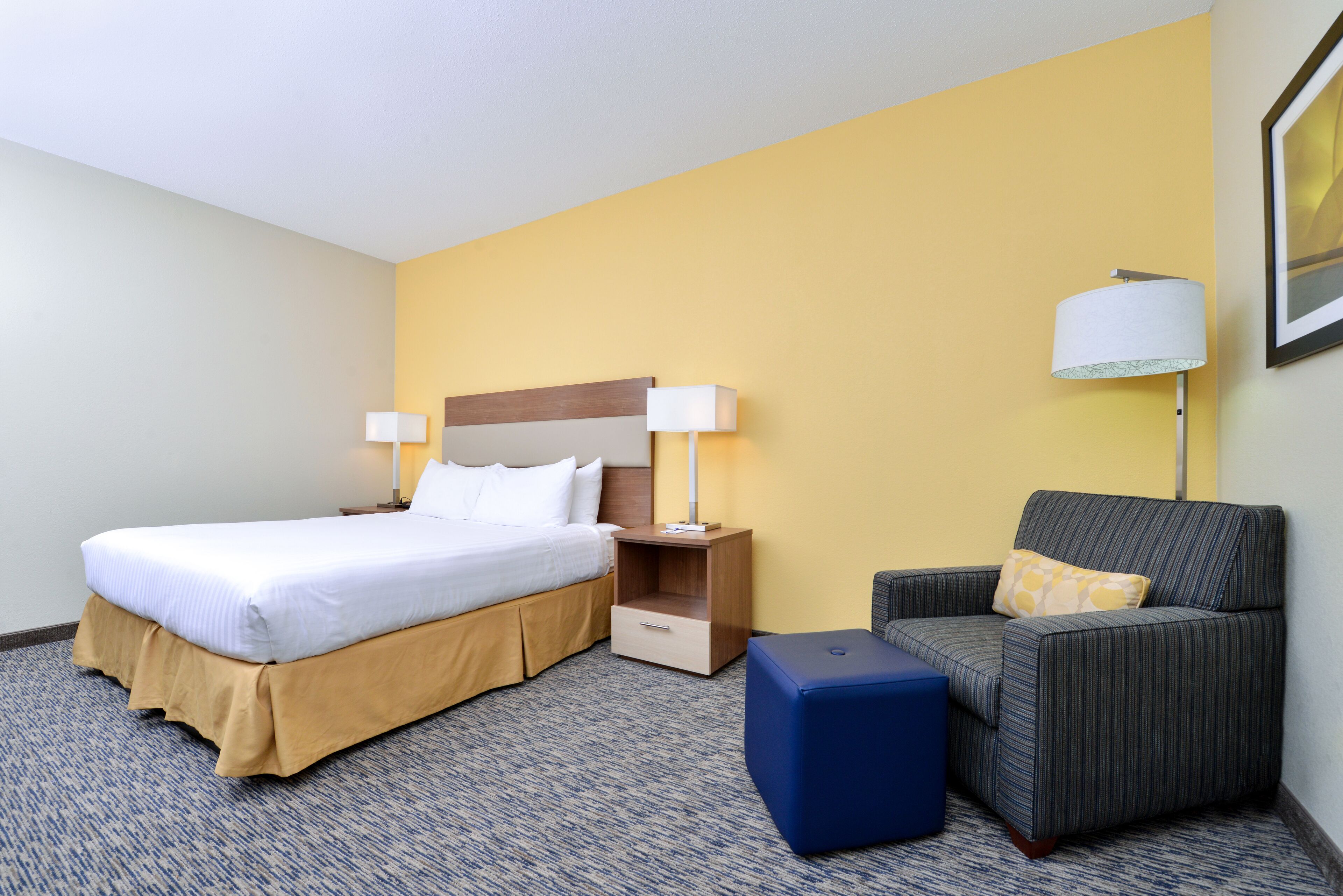 A hotel room with a bed, a nightstand with a lamp, a chair, and a small table.