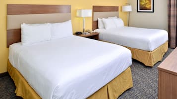 A hotel room with two beds, each with white linens and wooden headboards. There is a nightstand with a lamp and a phone between the beds. The room has a carpeted floor and a painting on the wall.