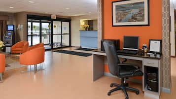 Zona de recepción de hotel con mostrador, computadora y dos sillones naranjas.