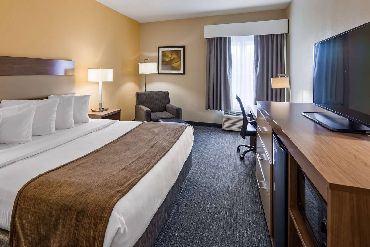 Ein Hotelzimmer mit einem großen Bett, einem Schreibtisch mit Fernseher, einem Sessel und einer Lampe.