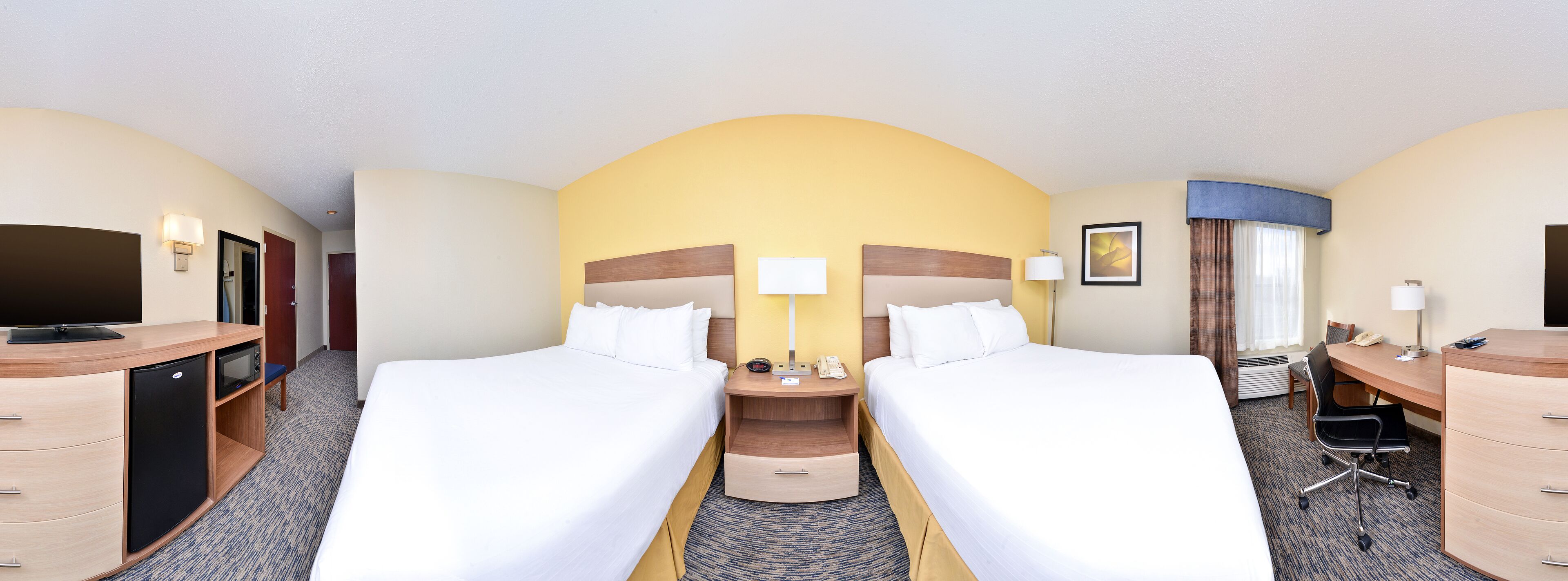 Une chambre d’hôtel avec deux lits, un bureau avec une chaise, une télévision, un mini-réfrigérateur et une lampe de bureau.