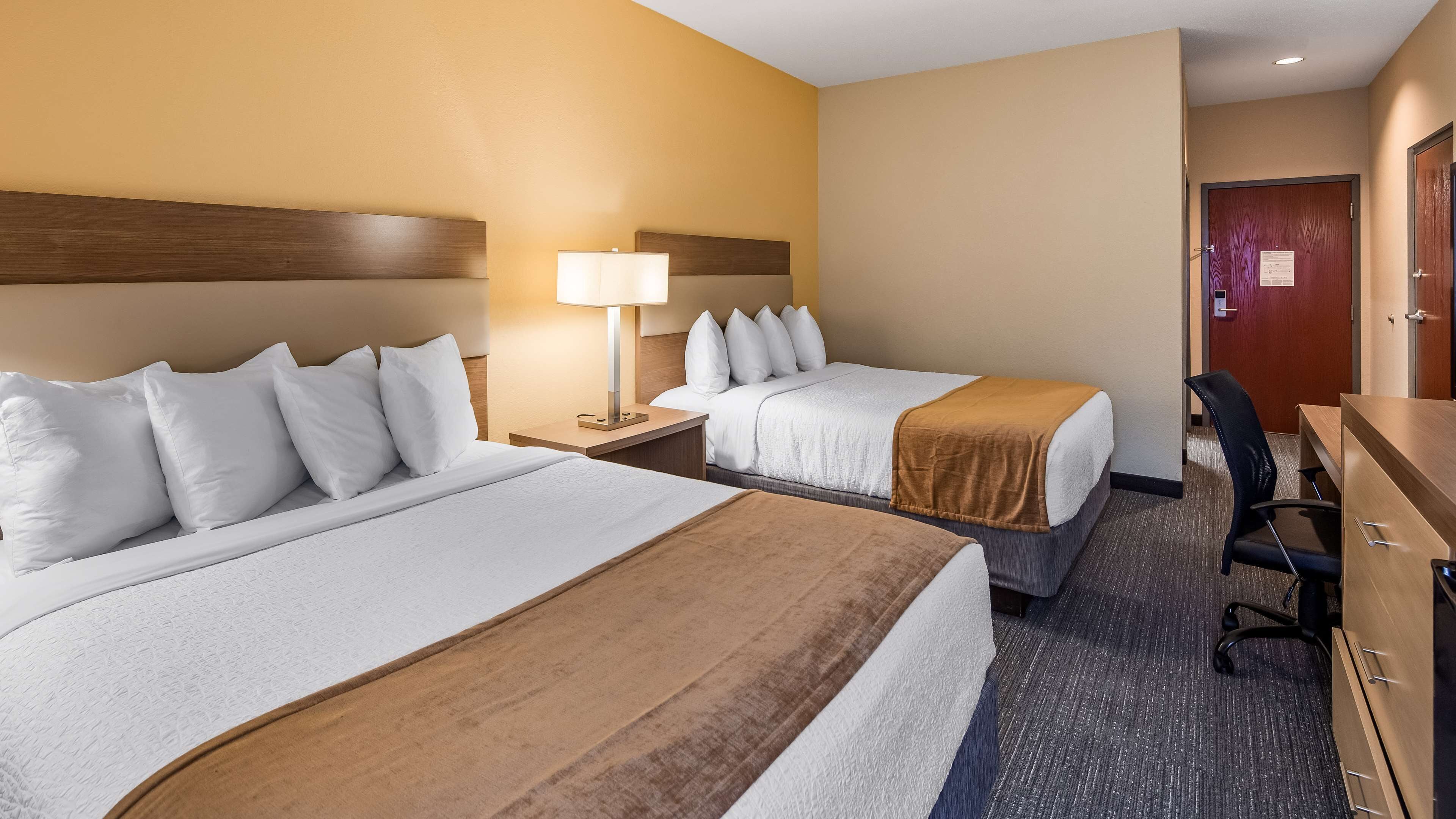 Une chambre d’hôtel avec deux lits, un bureau, une chaise et une lampe.