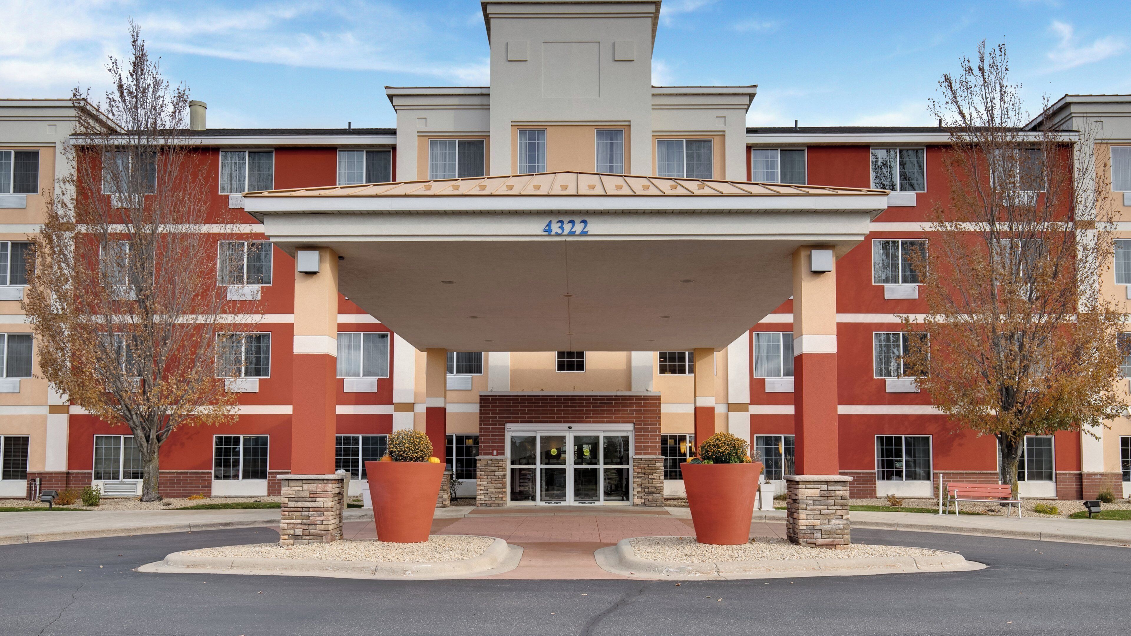 A multi-story building with a covered entrance, numbered 4322, featuring a brick facade and large potted plants at the entrance.