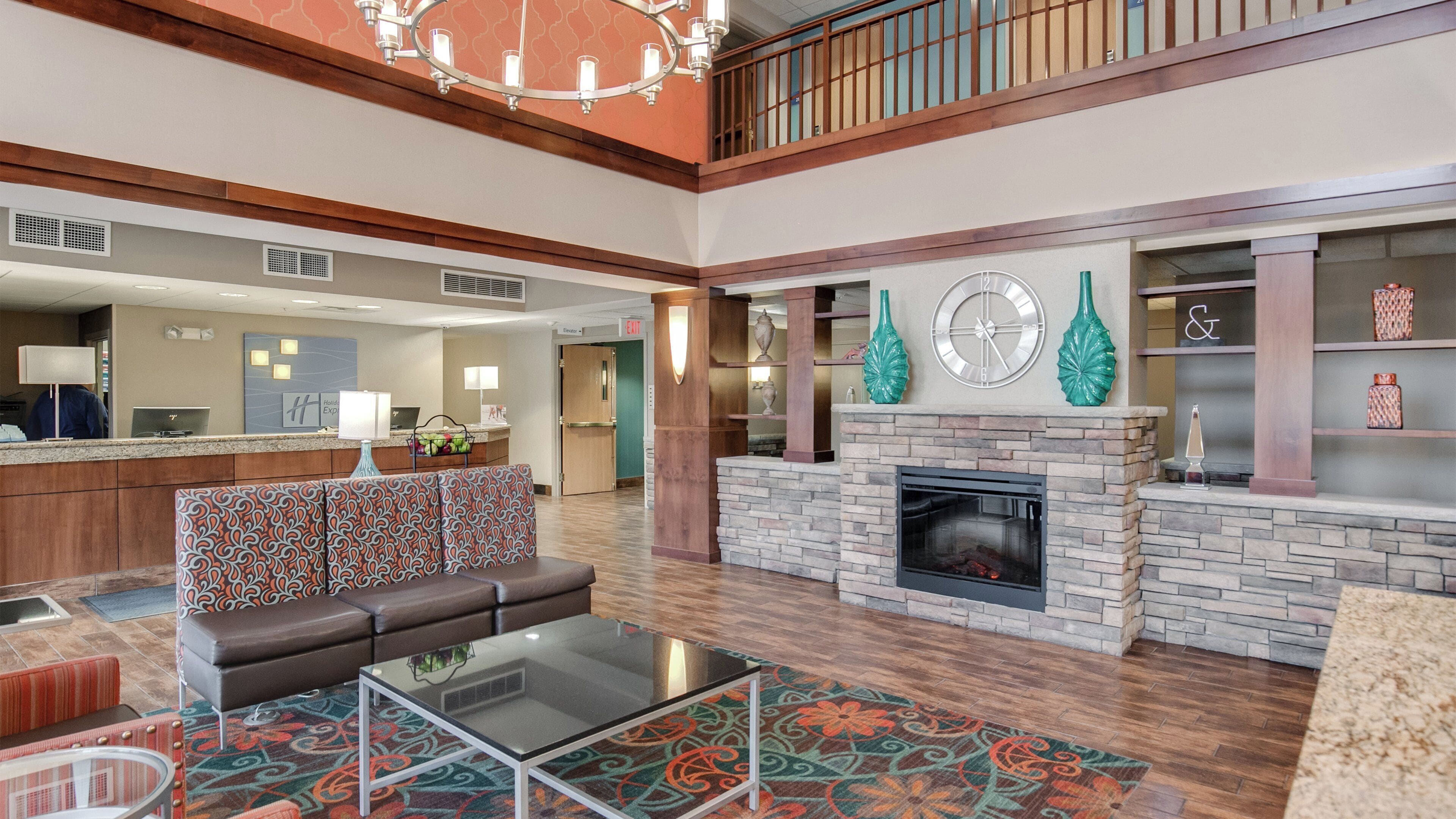 A hotel lobby with a reception desk, a fireplace, a seating area with a sofa and a coffee table, and a decorative wall with a clock and vases.