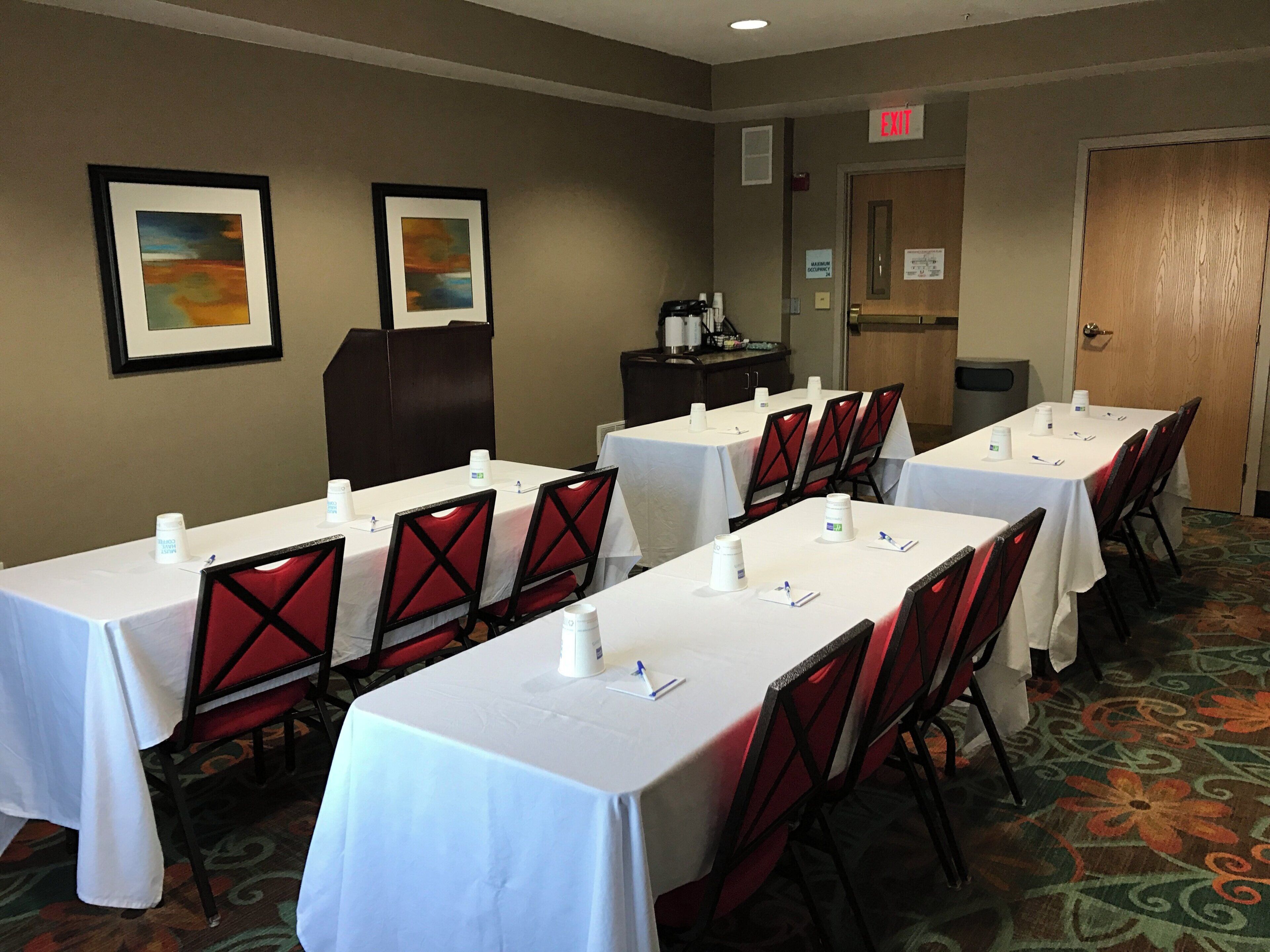 A conference room with tables and chairs, framed artwork on the walls, and an exit sign.