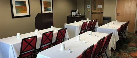 A conference room with tables and chairs, framed artwork on the walls, and an exit sign.