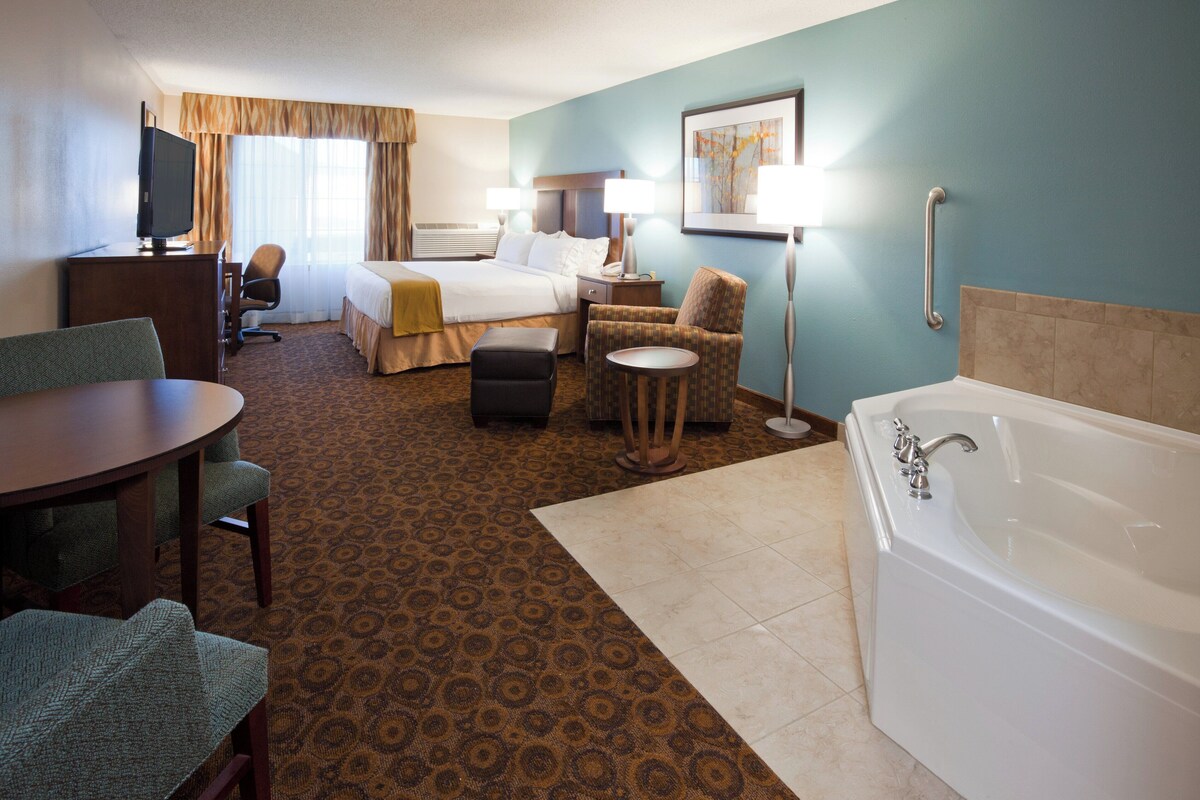 A hotel room with a bed, desk, chair, round table, and a bathtub.