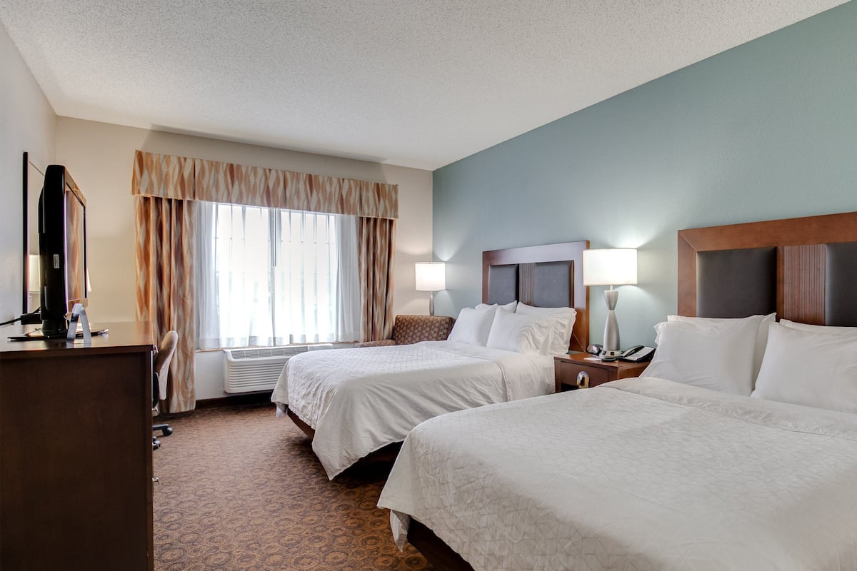A hotel room with two beds, a desk, a computer, and a window with curtains.