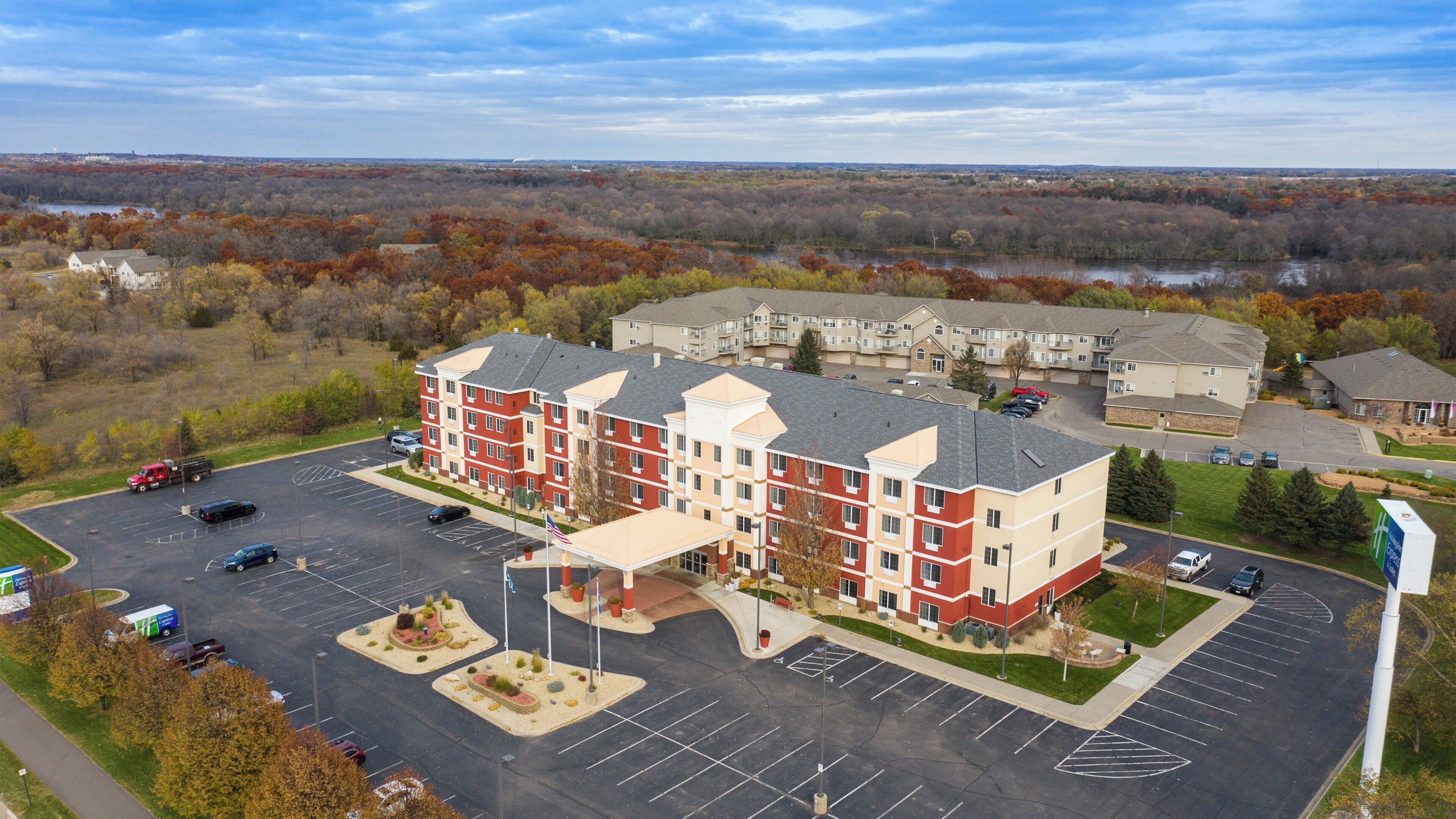 A multi-story hotel with a parking lot and a view of a lake and forest.