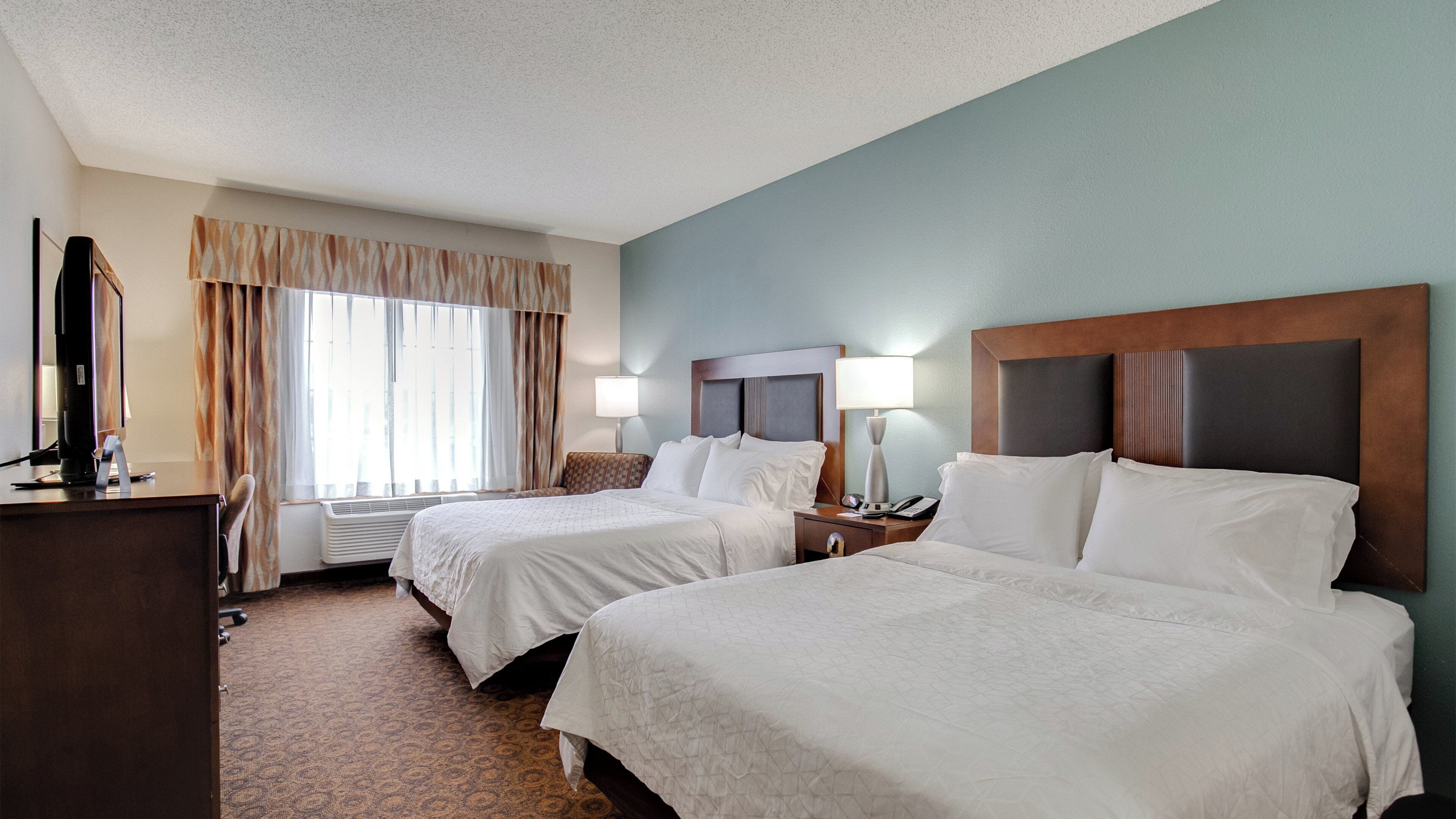 A hotel room with two beds, a desk, a computer, and a window with curtains.