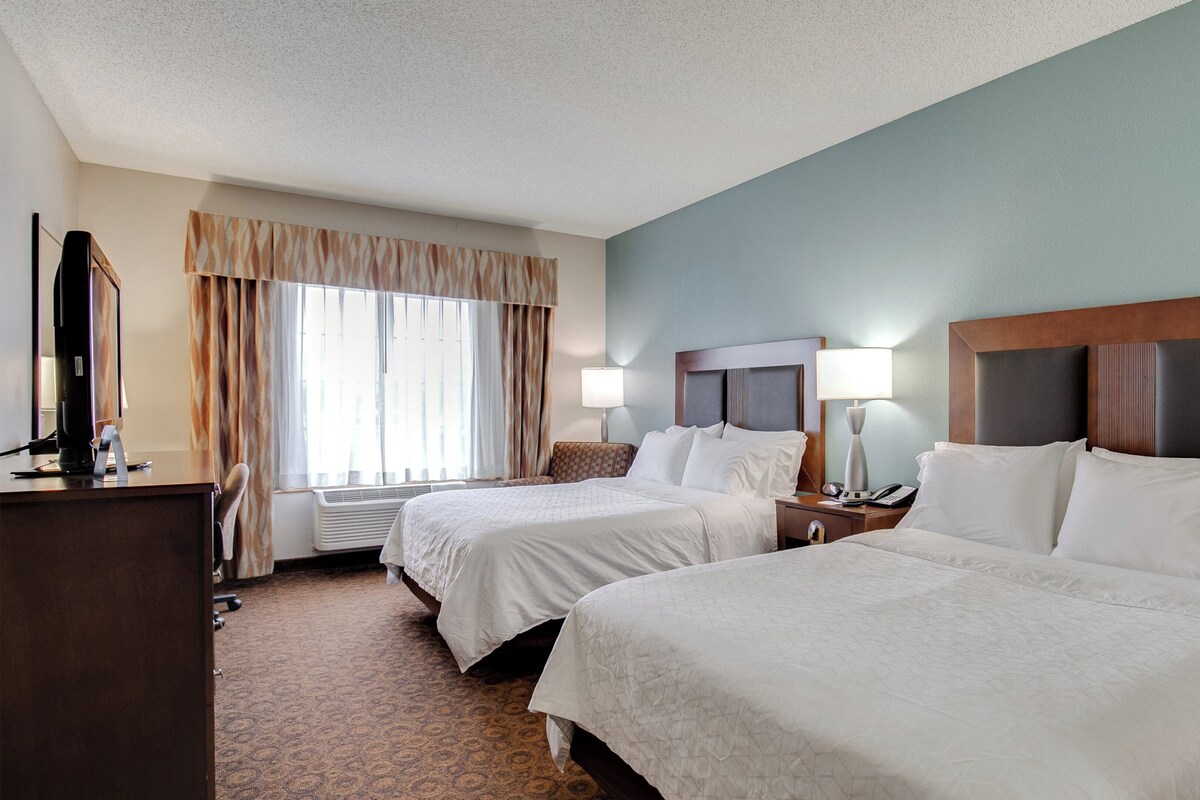 A hotel room with two beds, a desk, a computer, and a window with curtains.