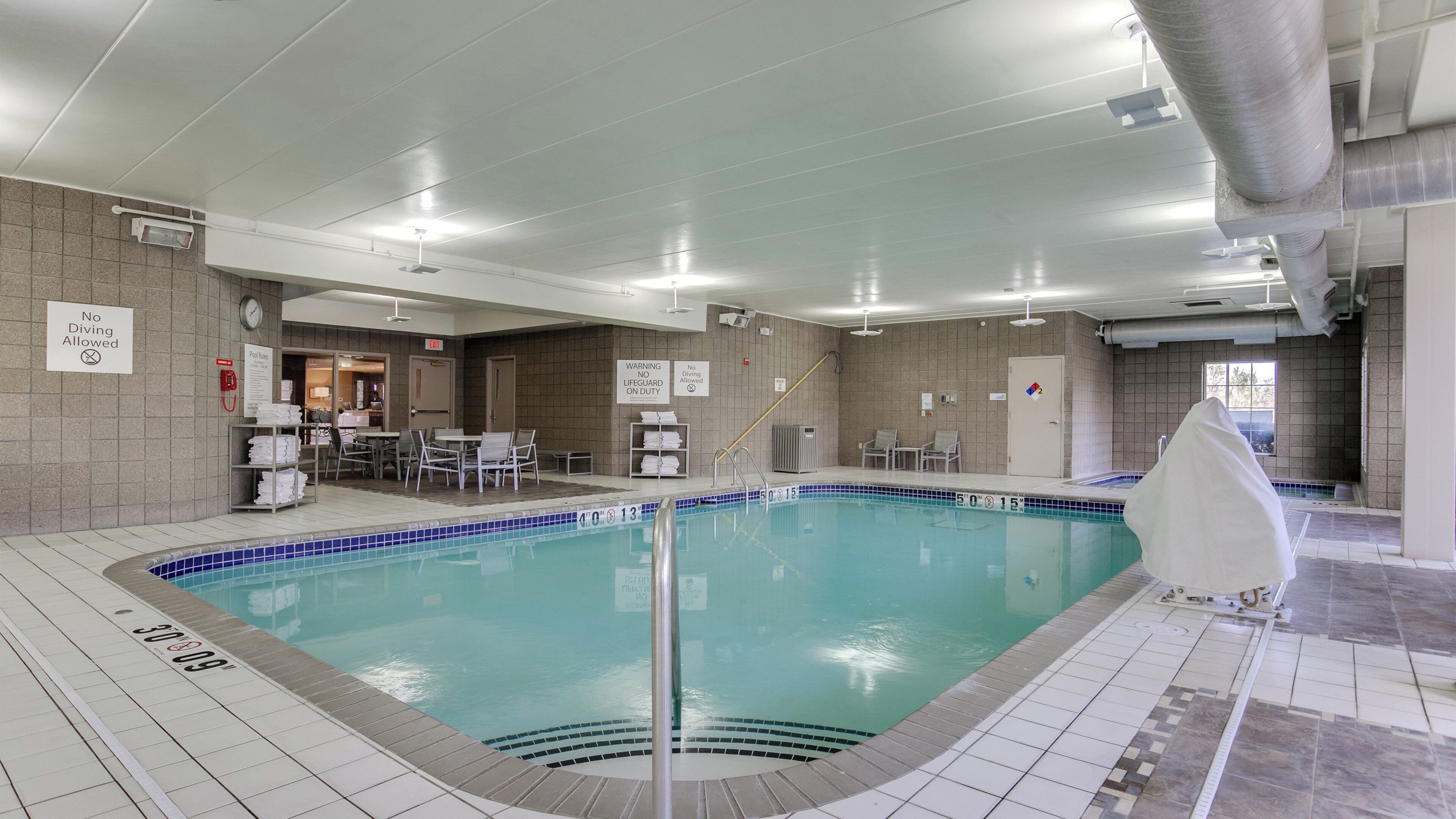 An indoor swimming pool with a lifeguard chair, pool rules sign, and a no diving allowed sign.