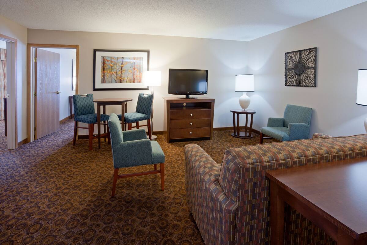 A hotel room with a TV, two armchairs, a sofa, a small table, and a lamp.