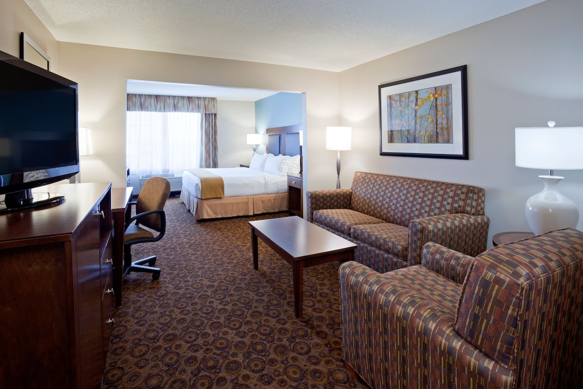 A hotel room with a bed, a desk with a television, a sofa, a coffee table, and a painting on the wall.