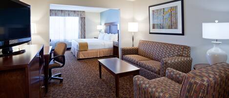 A hotel room with a bed, a desk with a television, a sofa, a coffee table, and a painting on the wall.