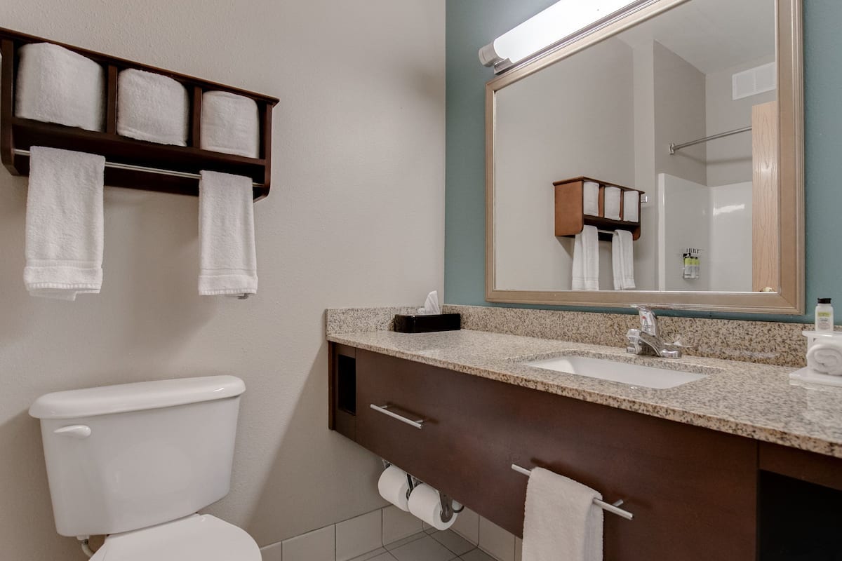 A bathroom with a toilet, sink, mirror, towel rack, and a shelf with towels.