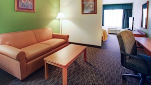 A hotel room with a sofa, a small table, a desk with a computer, a chair, two framed pictures on the walls, and a lamp.