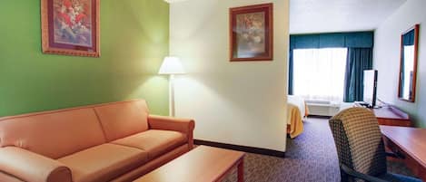 A hotel room with a sofa, a small table, a desk with a computer, a chair, two framed pictures on the walls, and a lamp.