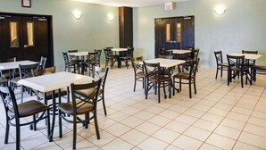 A dining area with multiple tables and chairs, light green walls, and ceiling lights.