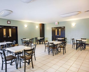 A dining area with multiple tables and chairs, light green walls, and ceiling lights. - Hotel Del Valle - Austin SE (Del Valle)