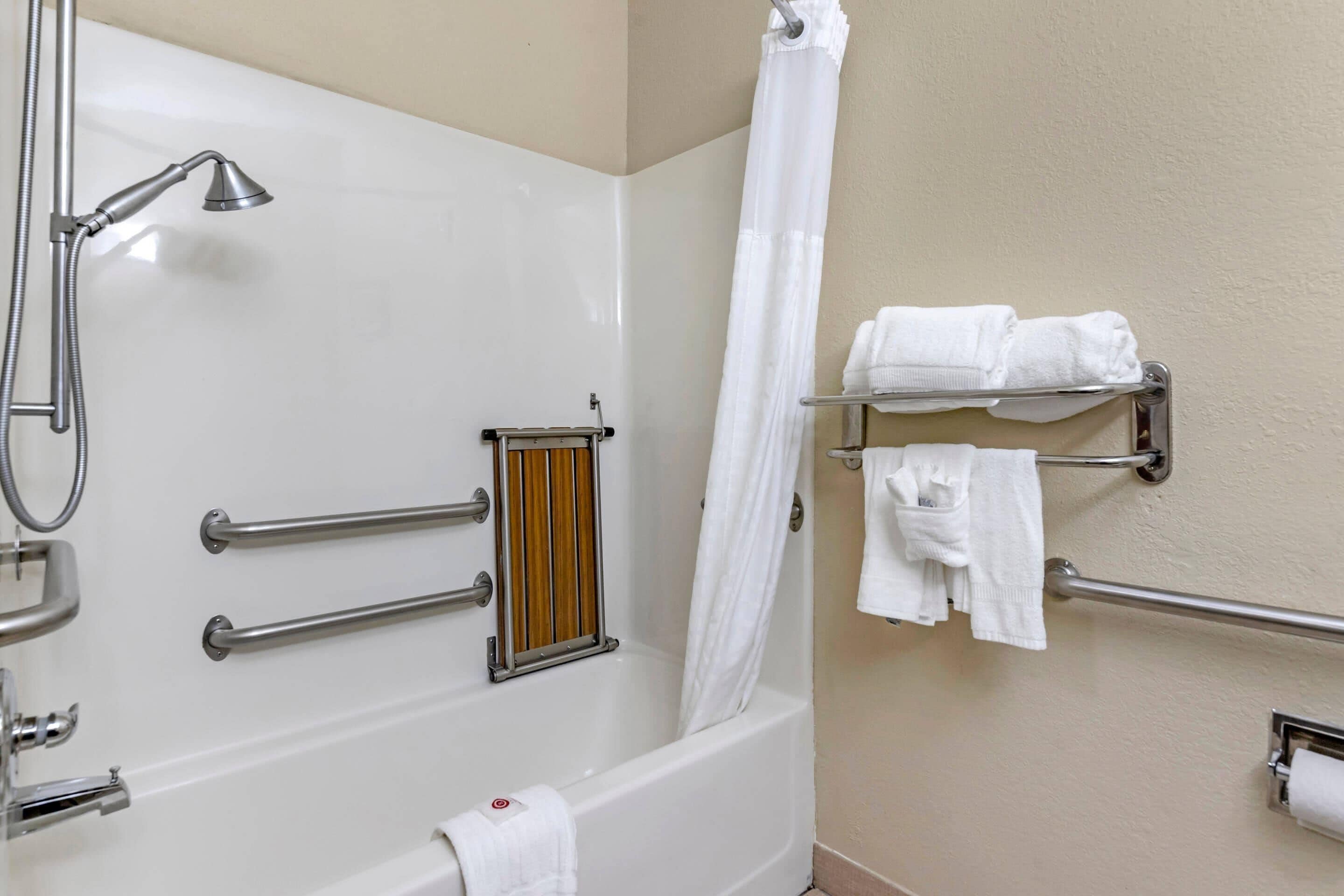 Un baño con bañera, ducha, barras de apoyo, toallero y soporte para papel higiénico.